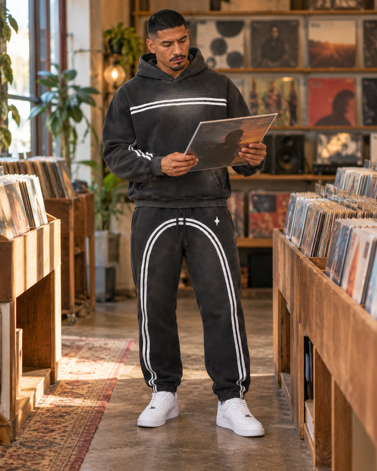 Male model wearing the black TLOL Threshold hoodie and matching joggers in a record shop